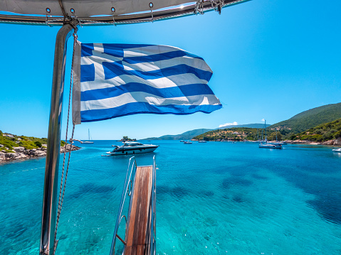 Greek flag on boat cruise around the island of Ithaki or Ithaca in the Ionian sea in the Mediterranean sea of Greece