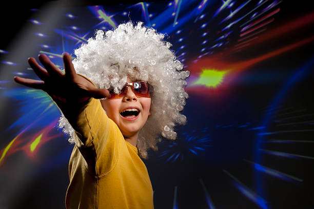 Child in glasses and a wig dances in disco lights stock photo