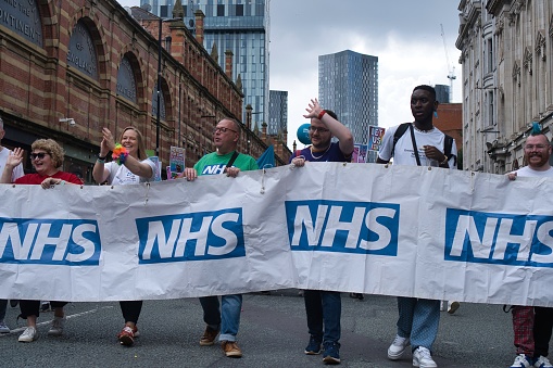 Photo of people parading on Deansgate ,Manchester for the annual gay pride 2023. Photo shot with Sony a6400, 35mm lens shows a group of people holding a large NHS banner.