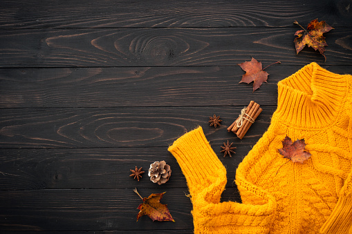Autumn background flat lay. Knitted sweater, fall leaves and spices on wooden background.