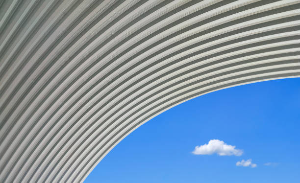 gran techo de cúpula curva de acero corrugado contra 2 mini nubes sobre fondo de cielo azul en estilo minimalista, vista de ángulo bajo con espacio de copia - industry aluminum sheet architecture metallic fotografías e imágenes de stock