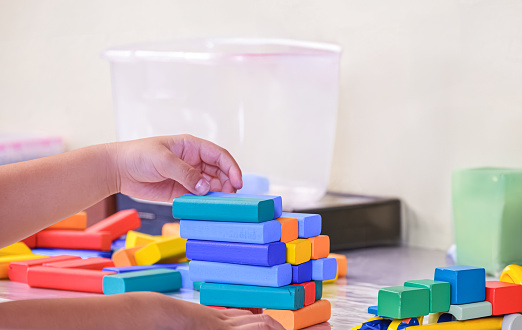 Close up image of child hands is playing colorful wooden blocks toy on table at home or kindergarten