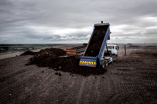A dumper truck unloading waste at a large waste dump with tailgate raised and unloading shredded waste at a landfill site with copy space