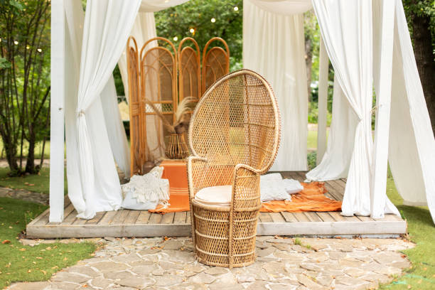 istock Rattan peacock armchair and decorative folding screen divider. Summer gazebo with flowing white curtains. Wedding boho decoration. Decor outdoor terrace with wicker furniture. Outdoor design of arbour 1640312477
