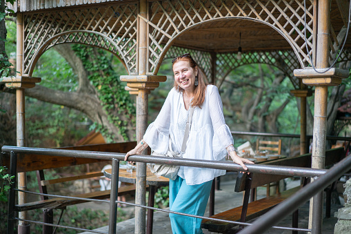 Beautiful smiling woman is standing by a wooden gazebo. People