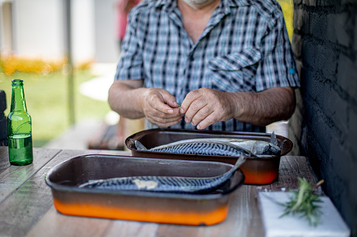 Senior man seasoning fish for barbeque in his back yard for a family event