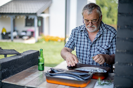 Senior man seasoning fish for barbeque in his back yard for a family event