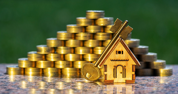 Pyramid of golden coins, miniature wooden house and golden key