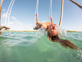 Young woman having fun on swing above a beautiful lagoon on a sunny day