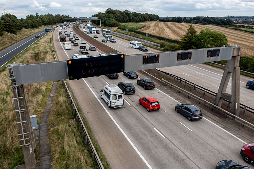 Leeds, UK - August 25, 2023.  An overhead warning sign on a busy UK managed motorway warning motorists to reduce speed and take caution because of a queue ahead on a busy Bank Holiday