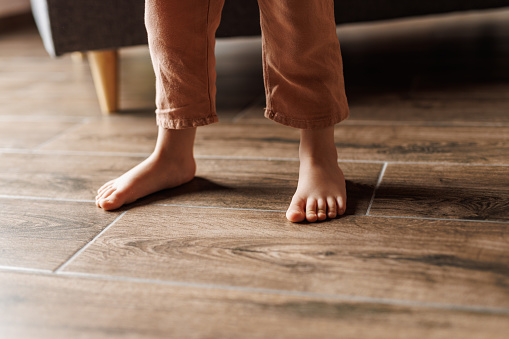 Low section of unrecognizable toddler barefoot walking on the floor. Part of a series.