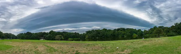 Shelf cloud (arcus) formed by the outflow of thunderstorms is approaching over a lake in a nature area.