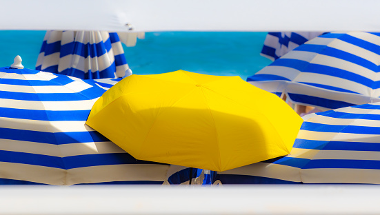 Un parasol jaune, sur la plage de Nice, contraste avec les autres parasols bleus et blancs.