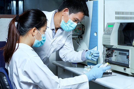 The male researcher checked the sample in the vial to analyze by Liquid Chromatography mass spectrometry LC-MS instrument in the laboratory and briefed a female scientist before analysis.