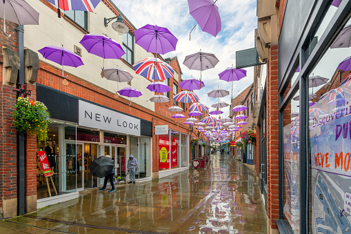 Purple umbrellas hang above the rainy wet, picturesque streets of shops, cafes and pubs in the historic old town center of the medieval city of Durham, England, United Kingdom. Durham is a city in northeast England, south of Newcastle upon Tyne. The River Wear loops around the Romanesque Durham Cathedral and Norman Durham Castle.