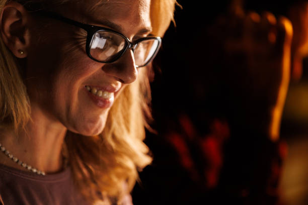 Close up shot of businesswoman smiling while using laptop at her desk late at night. Reflection of the screen seen in her eyeglasses.