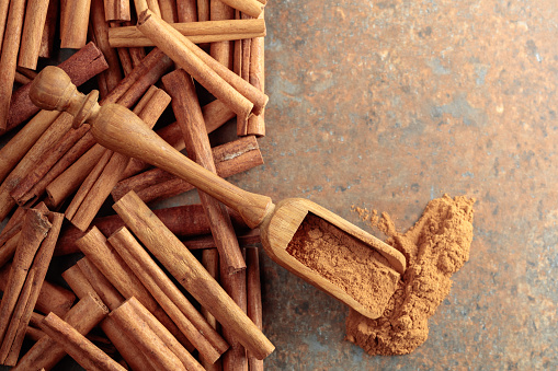 Cinnamon powder in a wooden spoon and cinnamon sticks on a rusty metal background. Top view. Copy space.