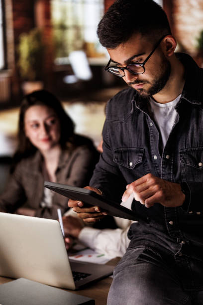 istock Young man sitting at the edge of a desk, using digital tablet 1640602273