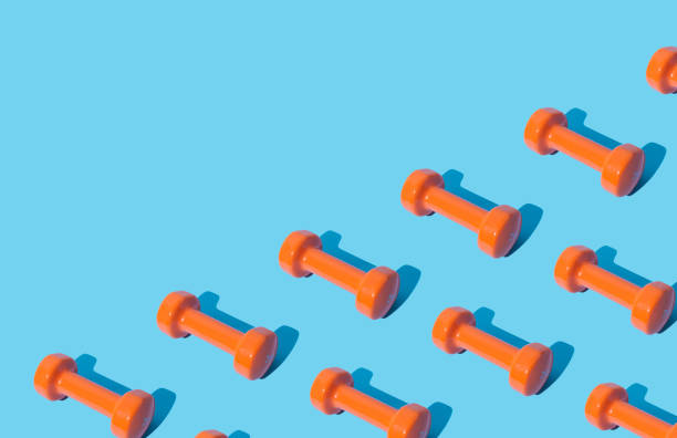 istock Creative pattern composition made of orange dumbbells on light blue background with copy space. Minimal fitness, healthy lifestyle and sport concept. Trendy exercise and fitness backround idea. 1640614499