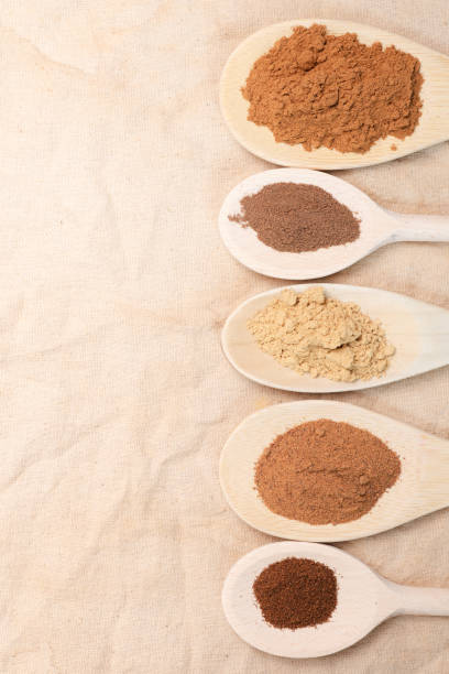 Spoons filled with ground spices to make pumpkin pie spice blend sitting on a rustic, wooden cutting board.