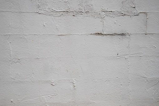 Weathered white block wall with grout patchwork, cracks, rough texture, and potential mold growth. Urban decay and neglect create a gritty backdrop.