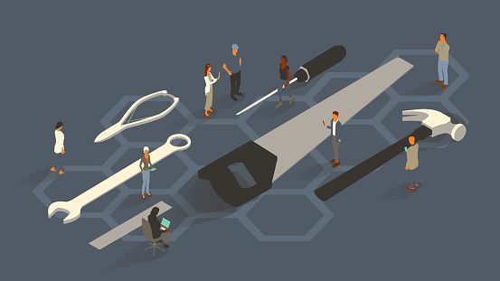 A group of nine people are dressed for business, illustrating the concept of business capabilities as they gather around an oversized set of hand tools including a screwdriver, saw, hammer, wrench, wire cutters, and ruler. Diverse men and women use digital devices. Isometric vector presented in a 16x9 artboard, over a slate gray background and a hexagonal honeycomb pattern.
