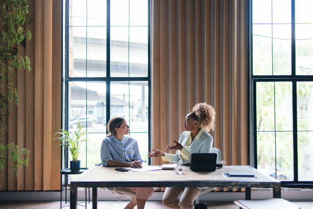 Two Successful Businesswomen Having a Meeting at the Office Two beautiful women sitting at the table, having a meeting at the office. They are talking and having a meeting, discussing projects and ideas. coaching stock pictures, royalty-free photos & images