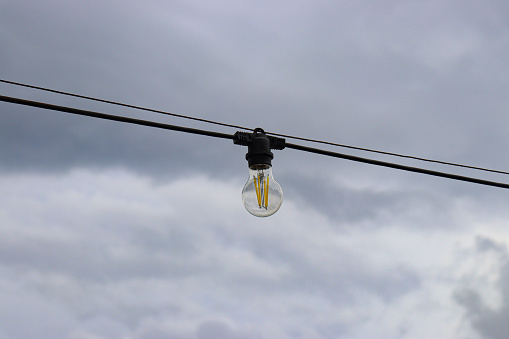 Light bulb hanging on electric cable outdoors on a cloudy day