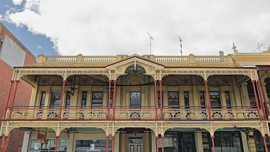 Mid-Victorian style heritage building from 1872: paired and sole Corinthian columns verandah, brackets-matching band, sunburst railing panels, central gablet balustrade parapet. Ballarat-VIC-Australia