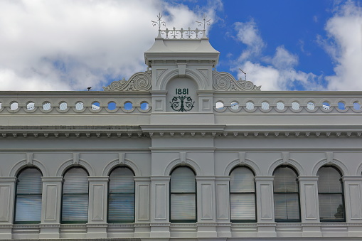 Renaissance revival building from 1881 featuring a round arched sash windows run, balustrade parapet and central gablet with lateral scroll decorations on clear-colored facade. Ballarat-VIC-Australia.