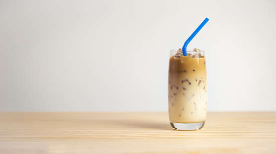 Iced coffee on wooden table, white background. Cold beverage in summer.