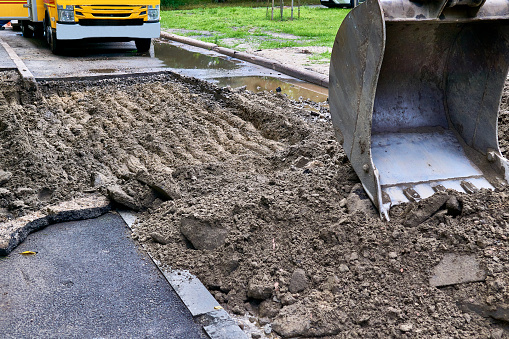 Excavator bucket picking up the ground, soil on road repair