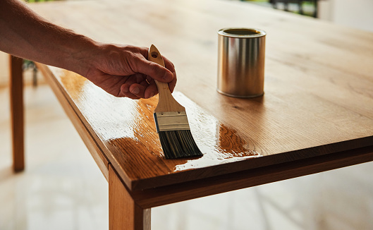 Closeup of man oiling wooden table with paint brush
