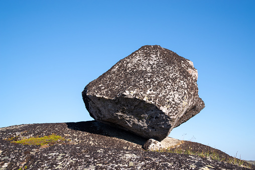 Large rock on a granite plate overgrown lichen. Clear blue sky background.