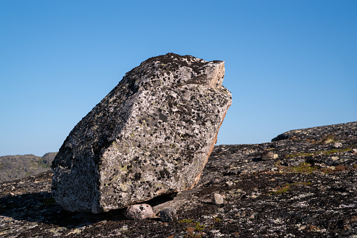 Large rock on a granite plate overgrown lichen. Clear blue sky background.