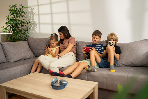 Mother and her three kids using phones while relaxing on couch at home