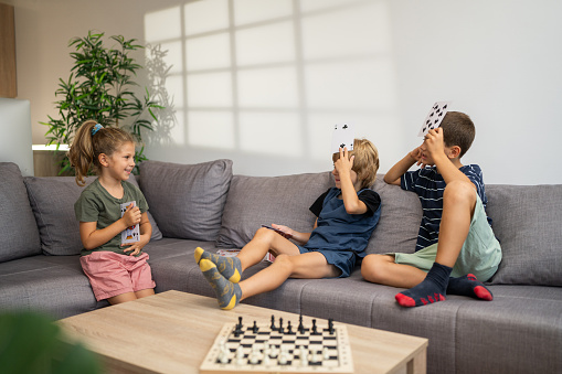 Cheerful kids, two brothers and sister playing with cards in living room at home