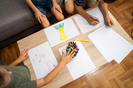 Close-up shot of three kids, two brothers and sister drawing together in living room at home