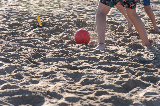 Children's feet playing soccer on the beach.