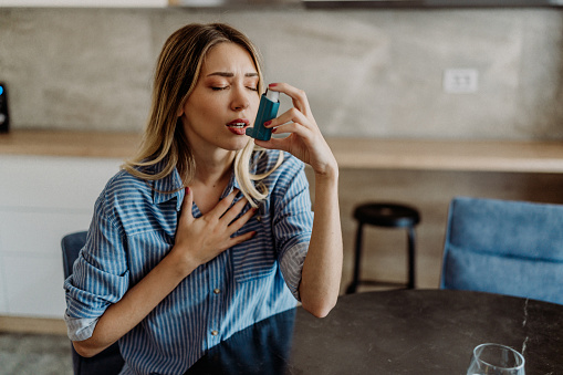 Young woman using her asthma inhaler at home