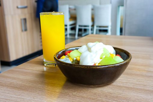 A bowl of fruit salad and glass of orange juice served on the table