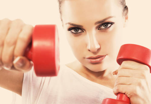 Attractive young woman is engaged in exercises with dumbbells. Authors color and added grain