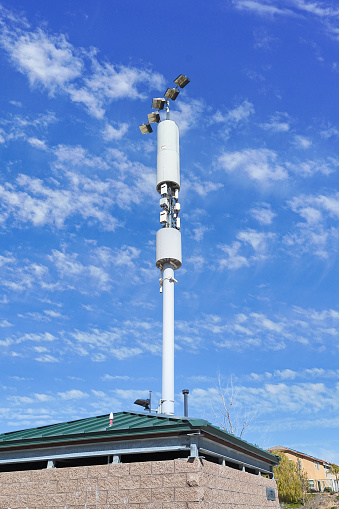 A cell phone tower and light tower next to a sports field