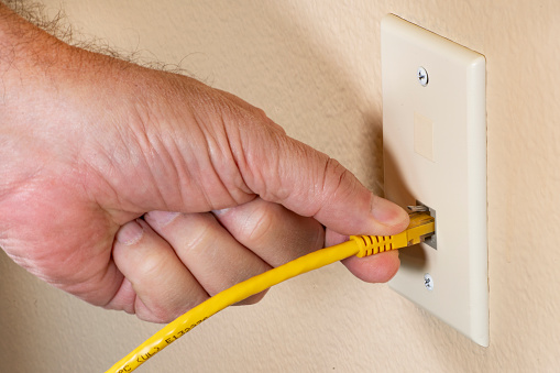 man's hand plugging yellow ethernet cable RJ45 into a home network socket