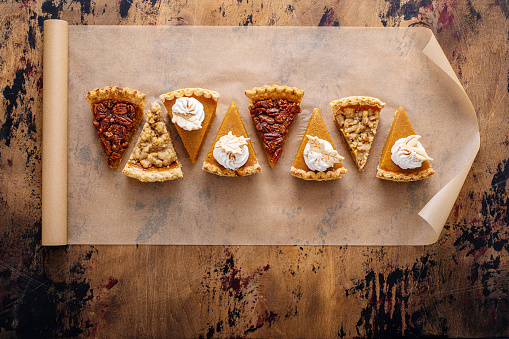 Traditional Thanksgiving pies cut into slices with pumpkin, pecan and crumble pies lined up on parchment paper