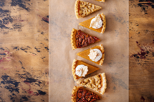 Traditional Thanksgiving pies cut into slices with pumpkin, pecan and crumble pies lined up on parchment paper