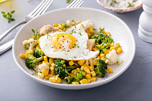 Healthy breakfast bowl with cooked vegetables and fried egg, with cauliflower, broccoli and corn
