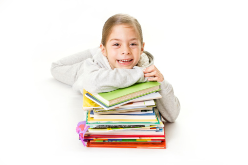 A happy little girl who enjoys reading smiles while sitting with her pile of books