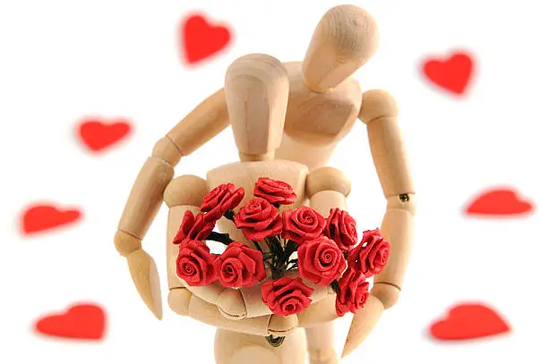 Wooden Mannequins showing their love. Situation of boy holding girl in his arms. Woody ifn front holding bunch of roses. in background red hearts. focus on roses. perfect valentines day background and wedding.