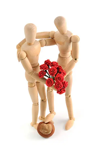Wooden Mannequins showing their love. two wooden mannequins holding each other in arm with a bunch of roses in hand. the foot stands on a chestnut witfh heart shape. the triumph of love. focus on roses. perfect valentines day background.